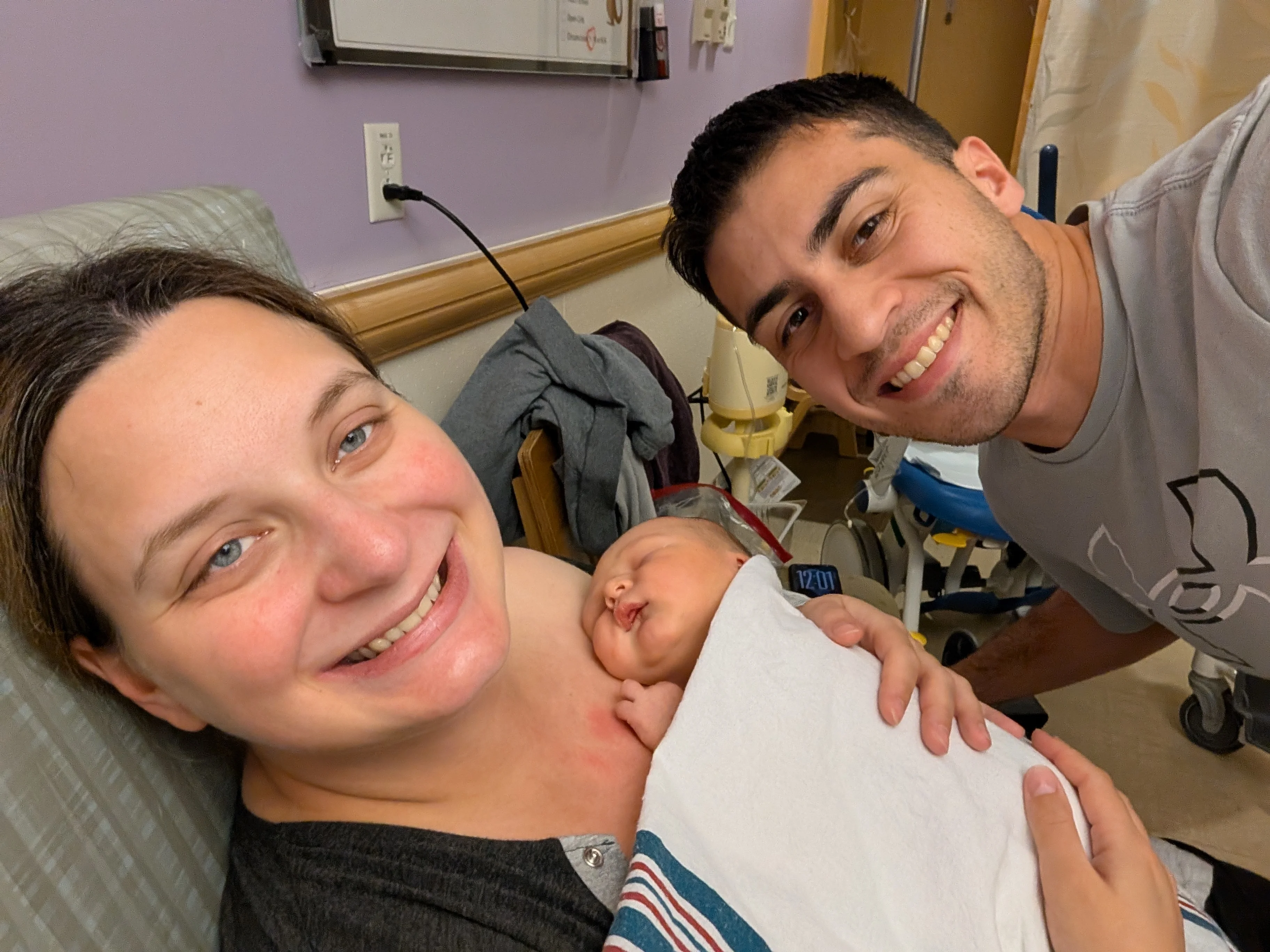 Amanda in a hospital bed holding newborn Nolan on her chest, with Mark leaning in beside them, both smiling.