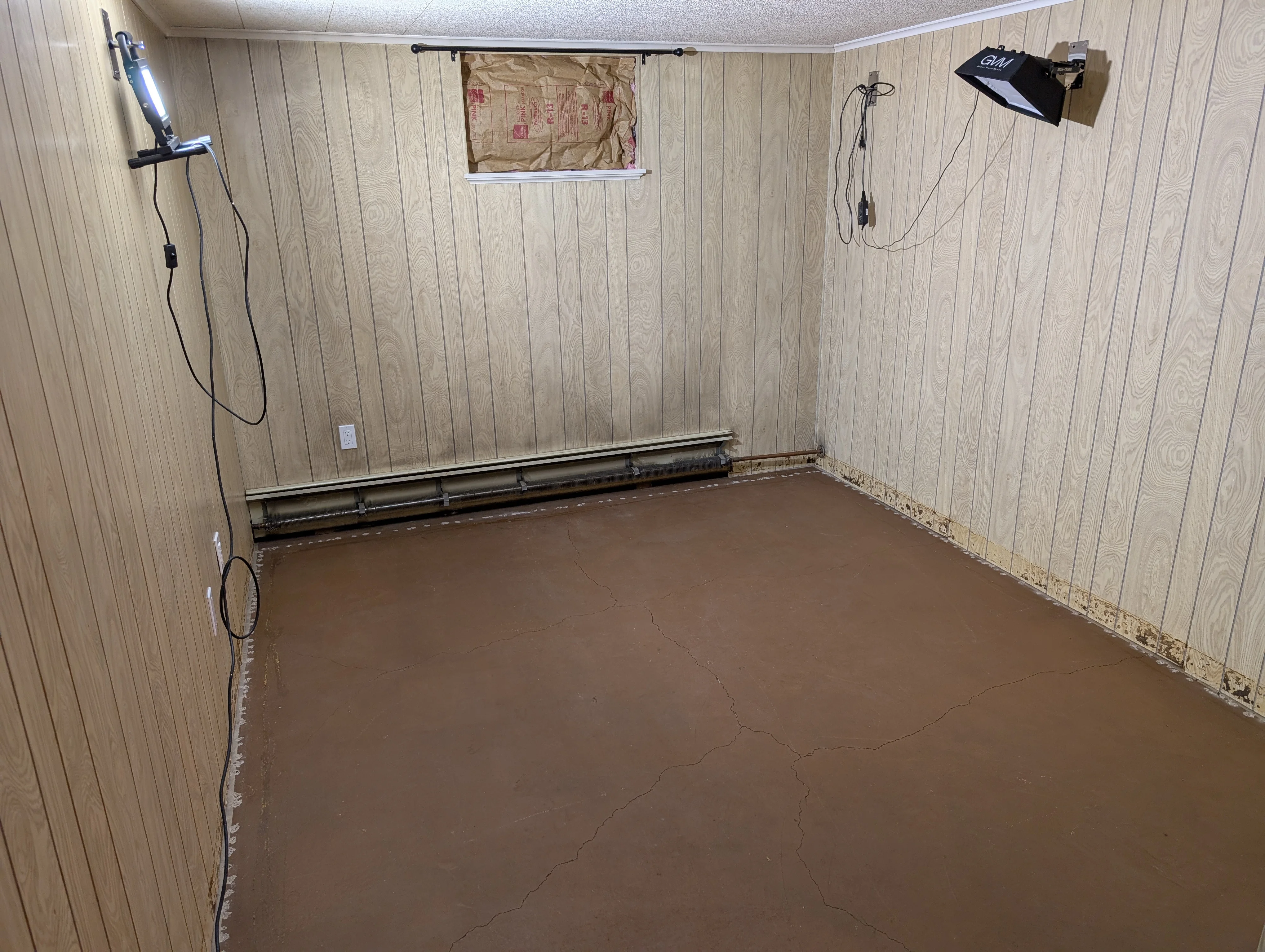 The empty basement room before the build: wood paneling, a bare cracked concrete floor, and an old baseboard heater.