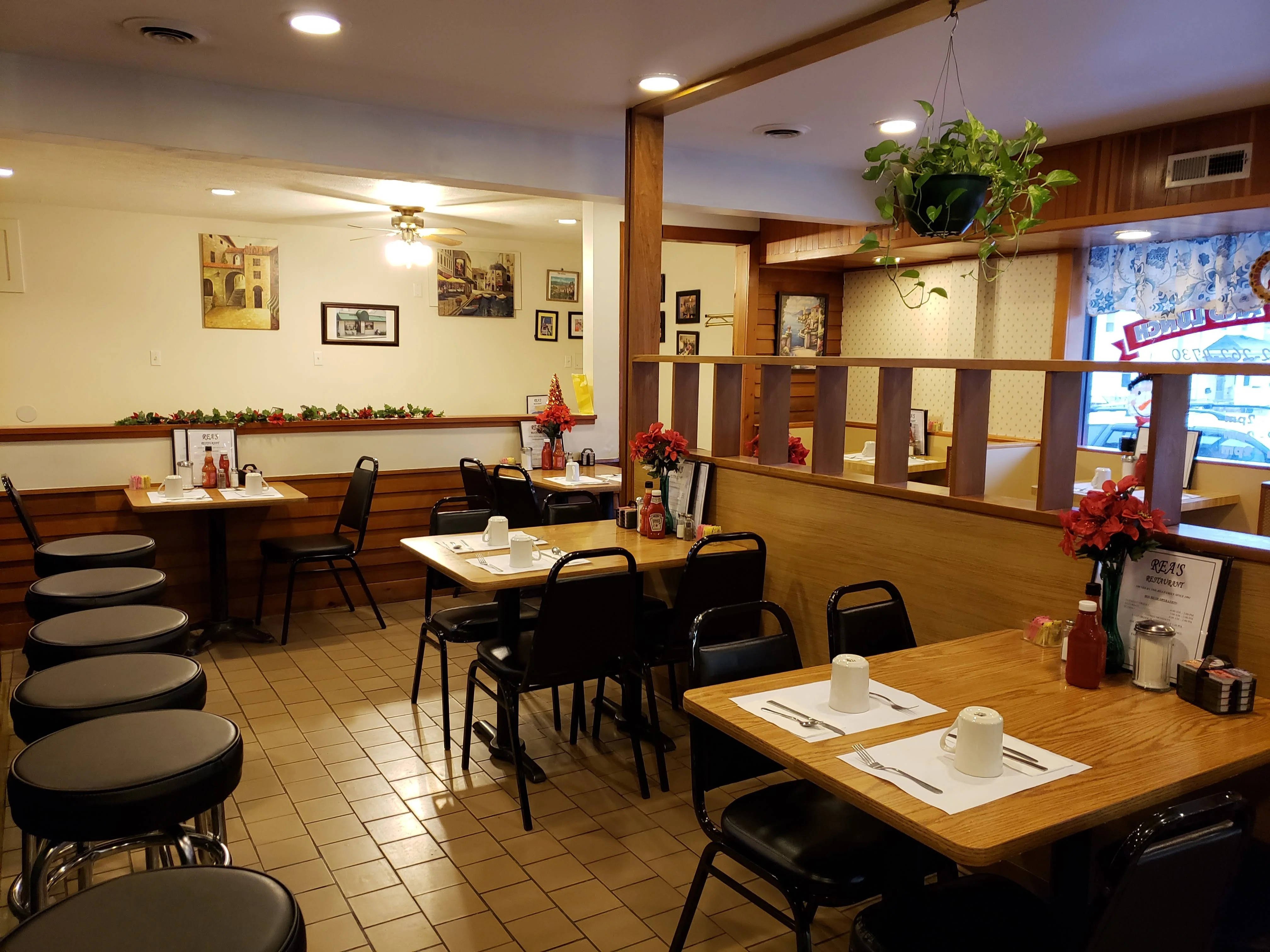 The inside of Rea's Restaurant: wooden tables set with mugs, a row of counter stools, and Italian paintings on the walls, decorated for Christmas.