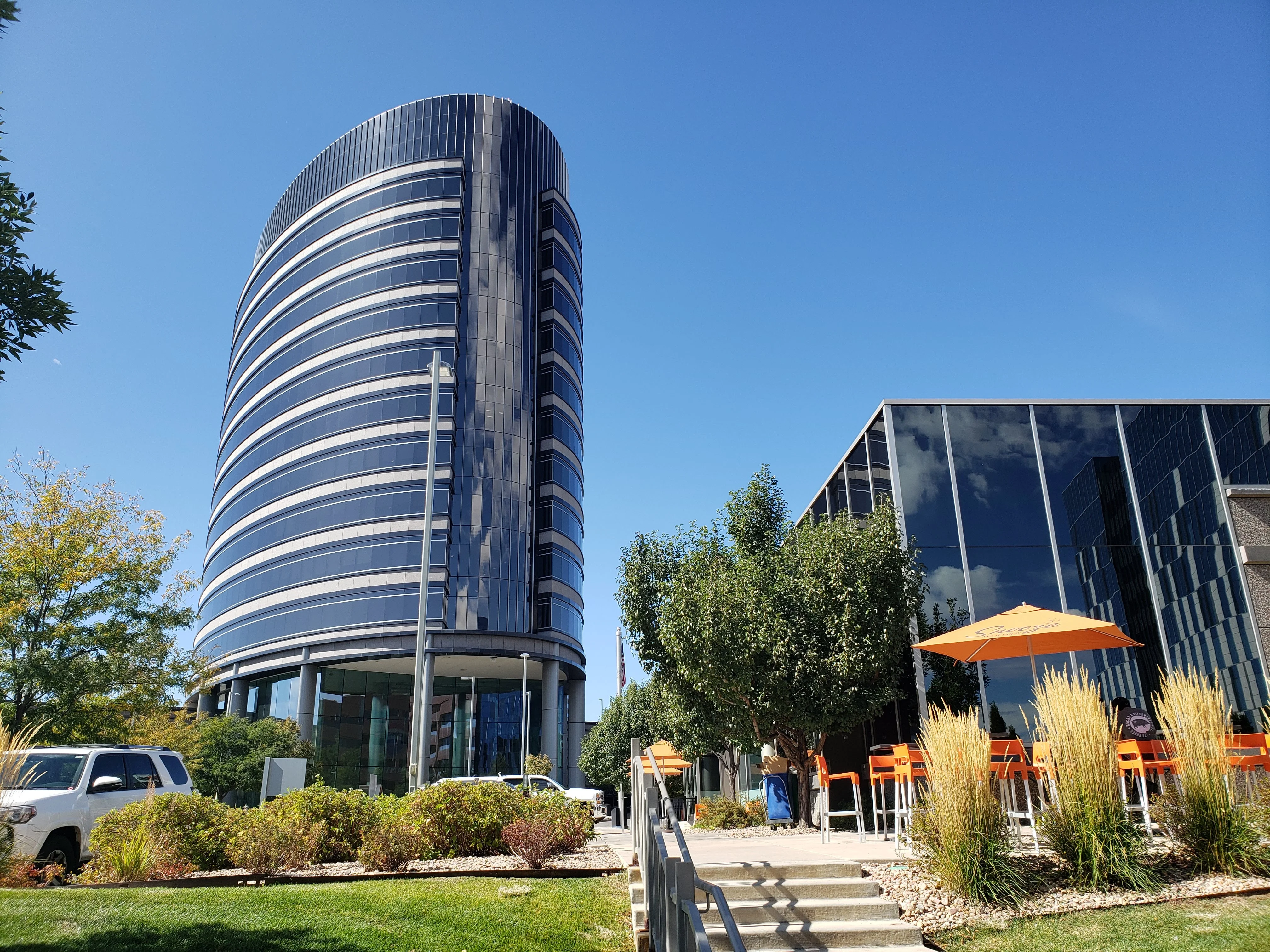 The curved glass tower of RE/MAX world headquarters in Denver under a clear blue sky.