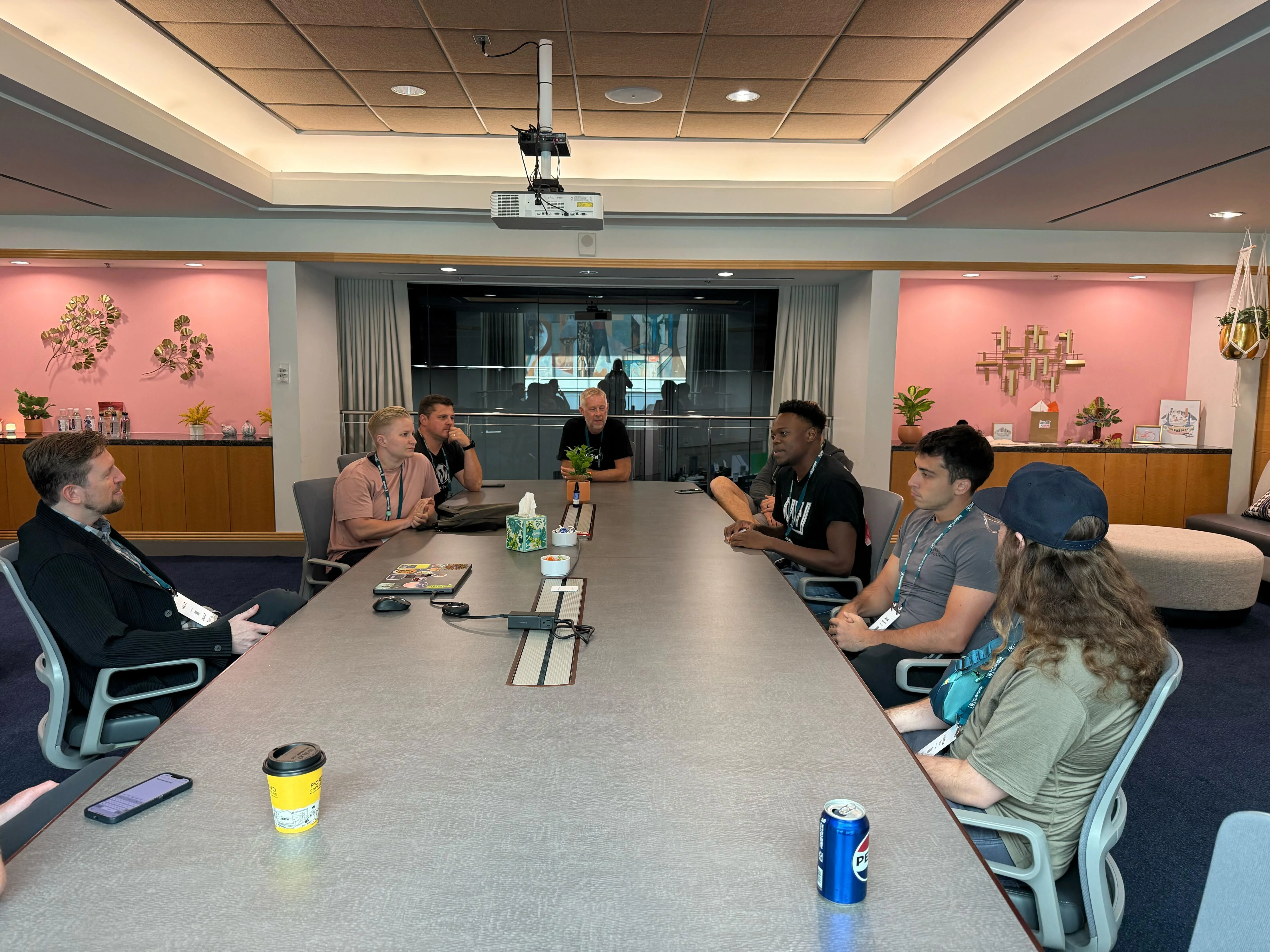 A conference room meeting at WordCamp US 2025, seen down the length of the table, with members of the Automattic team seated around it.